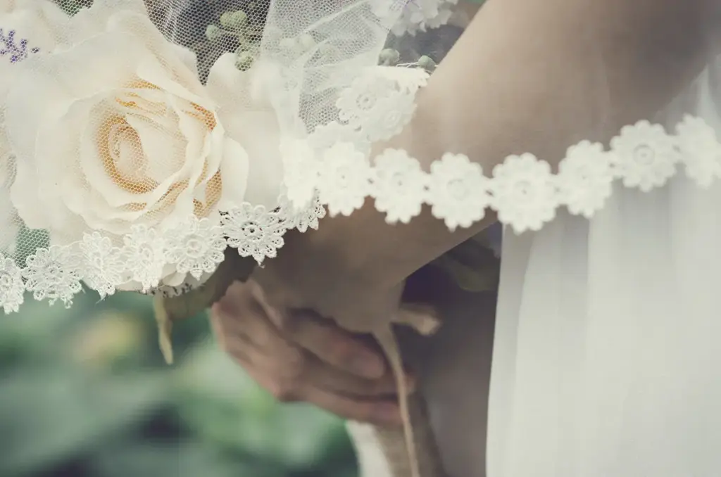 Brautstrauß mit hellen Rosen vor einem Hochzeitskleid aus Spitze
